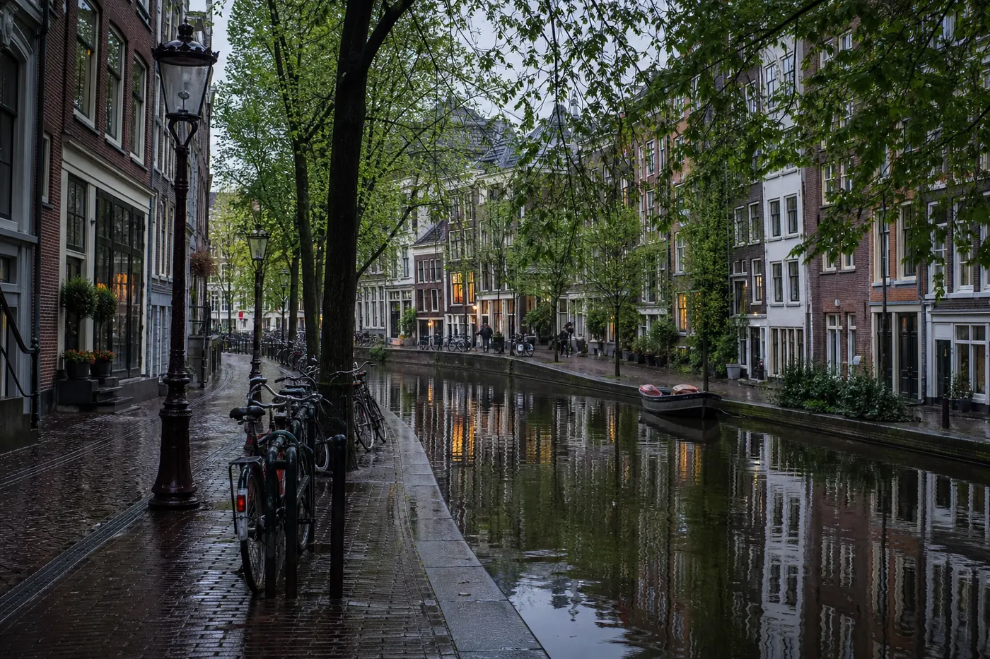Amsterdamse gracht met natte kade, fietsen en weerspiegelingen na een regenbui